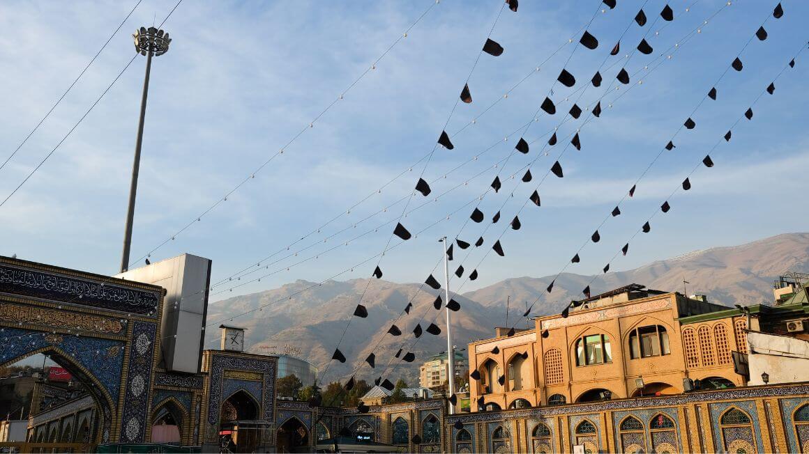 flags hanging from a mosque site with a mountain backdrop in tehran, iran