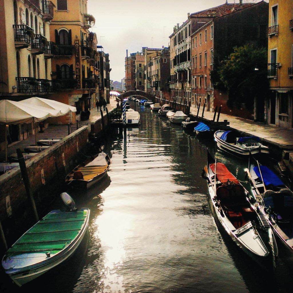 A canal in Venice Italy filled with gondolas and small boats lining old aesthetic buildings