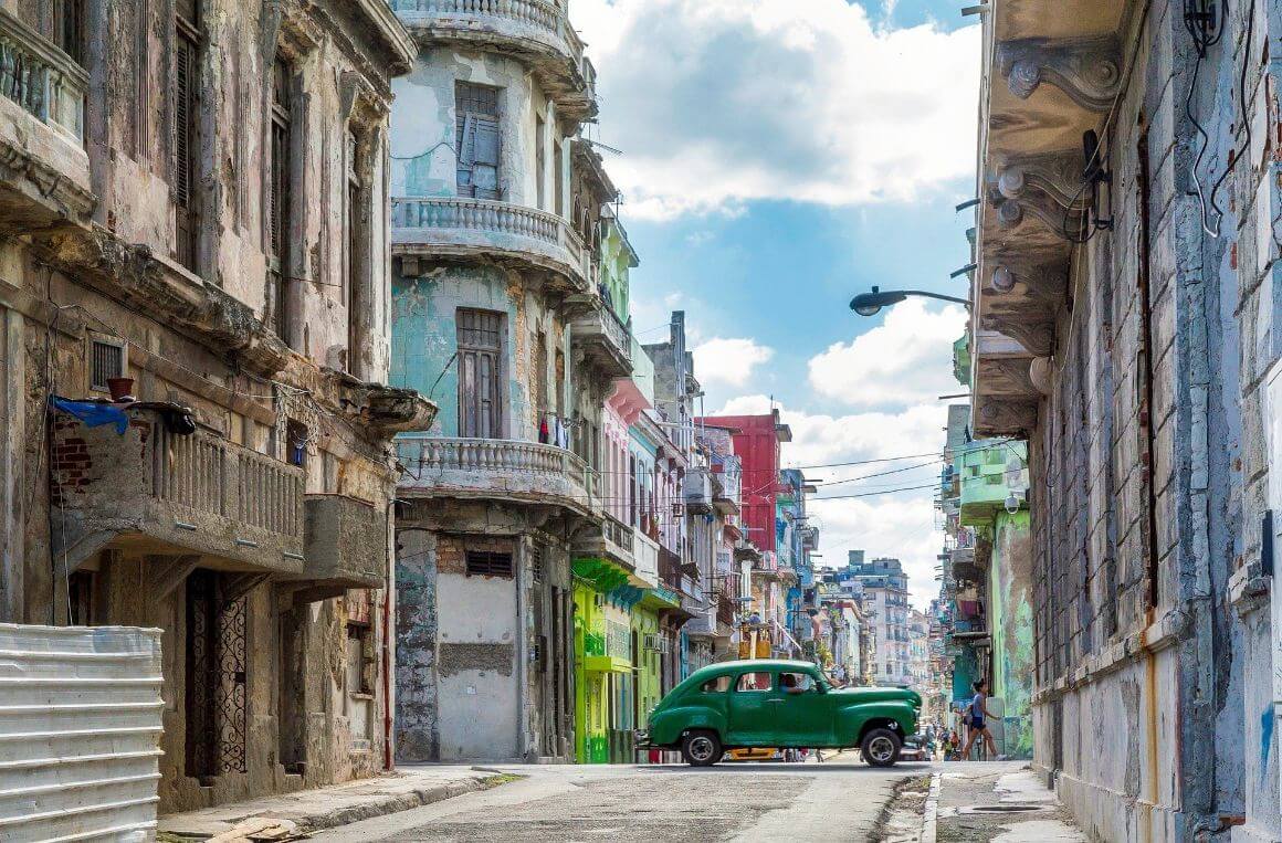 a vintage green car drives through central habana streets