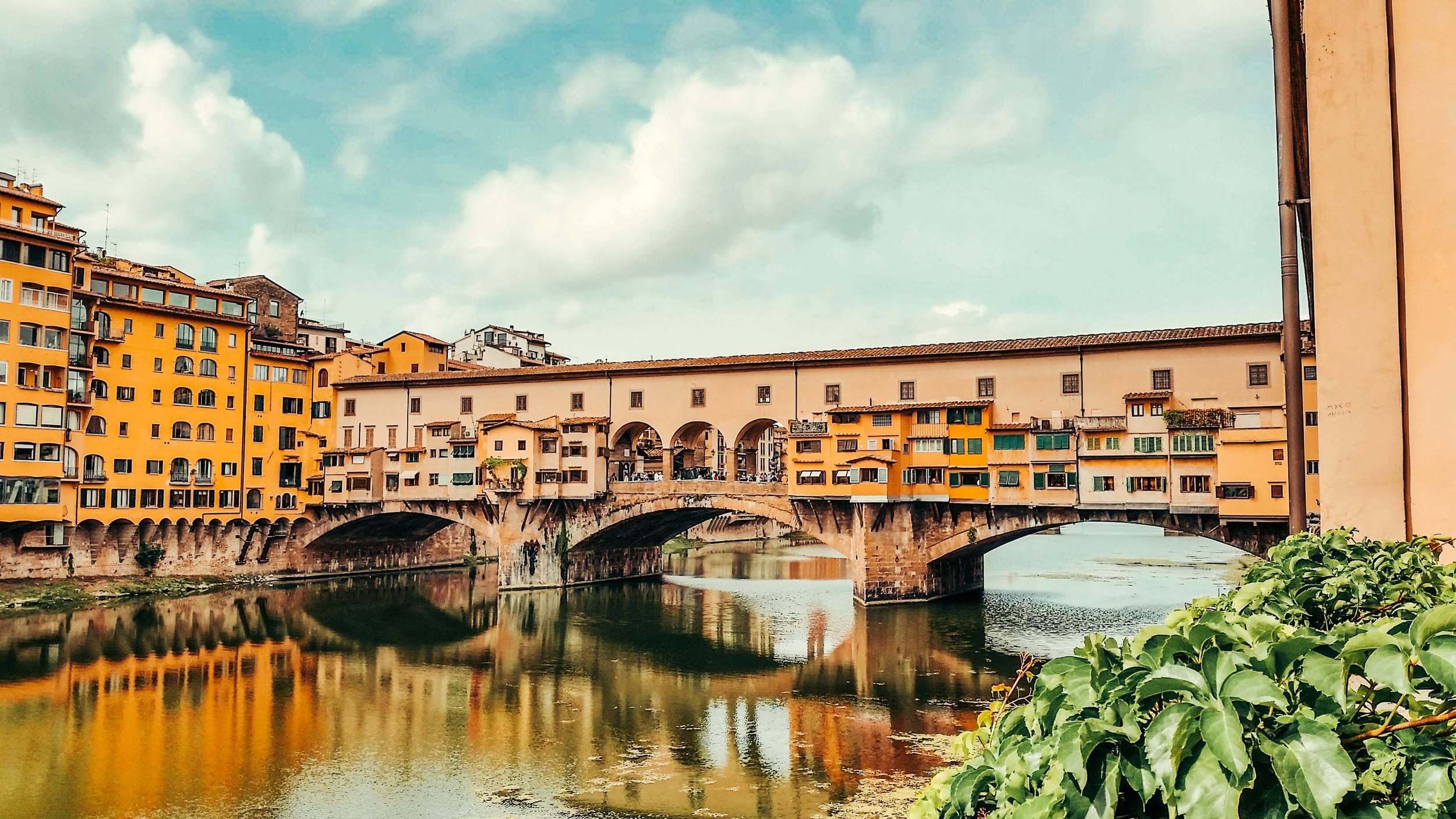 a light pink and orange bridge with multiple layers crossing a river in florence italy