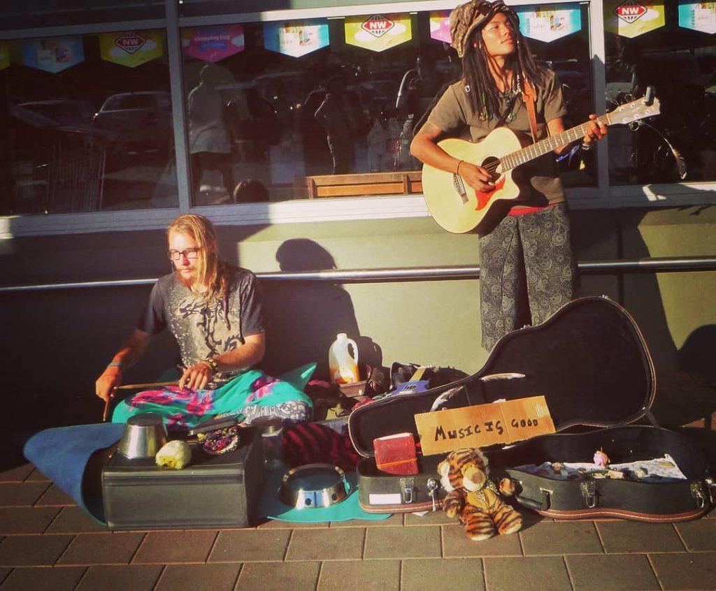 Two travellers busking, one with his portable guitar