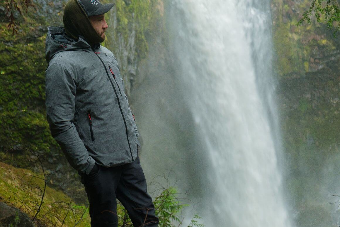 A person standing next to a waterfall in a waterproof jacket