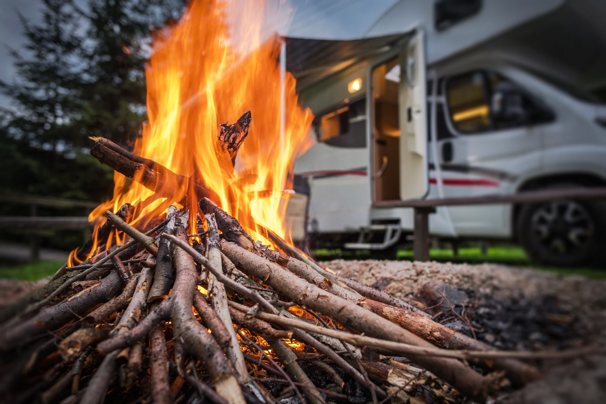 A campfire in front of a parked motorhome in an RV campground