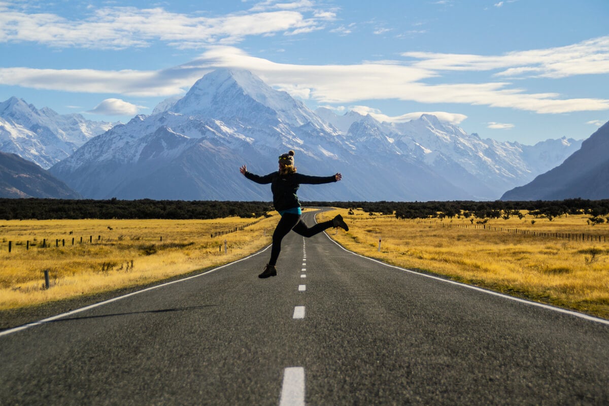 Woman jumps for joy on the road driving to Mount Cook in South Island 