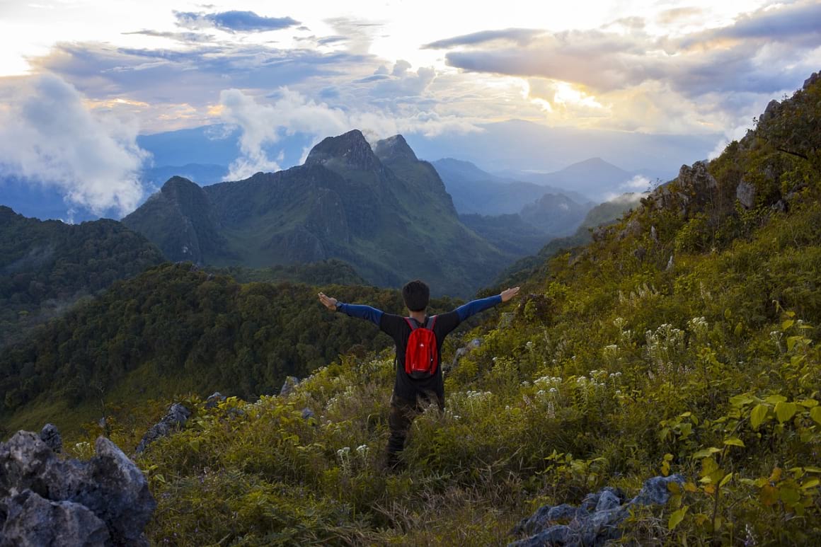 A person standing in a mountain in Doi Chiang Dao, carrying a red backpack and outstretching his arms 