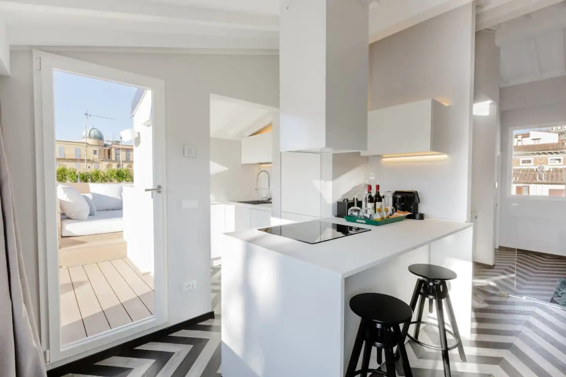 Modern kitchen. White and black interior design. Door that leads out to a terrace with comfy outdoor furniture.