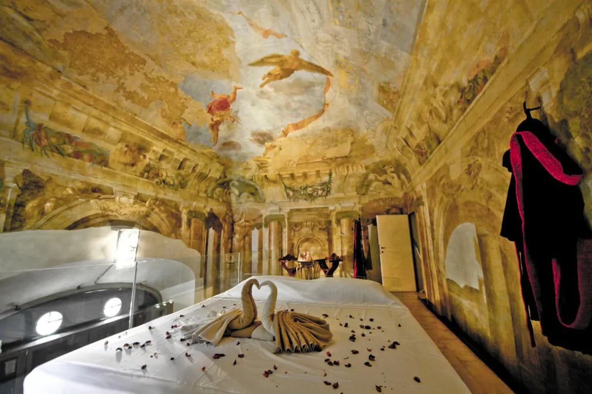 Renaissance styled bedroom with artwork covering the walls. Bed in the centre of the room covered in rose petals. 