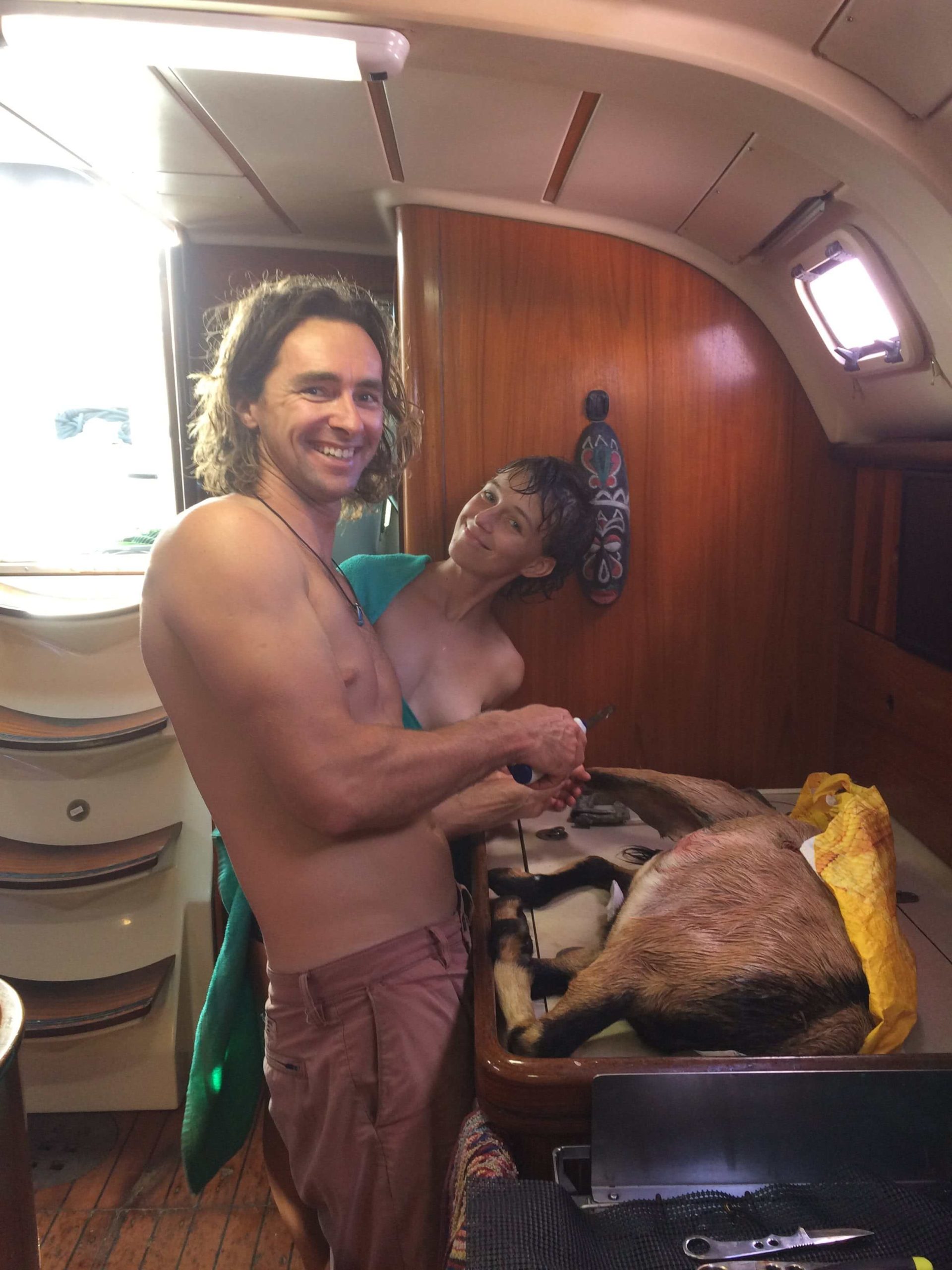 A man and a woman on their liveaboard sailboat. A goat they killed is in front of them. 
