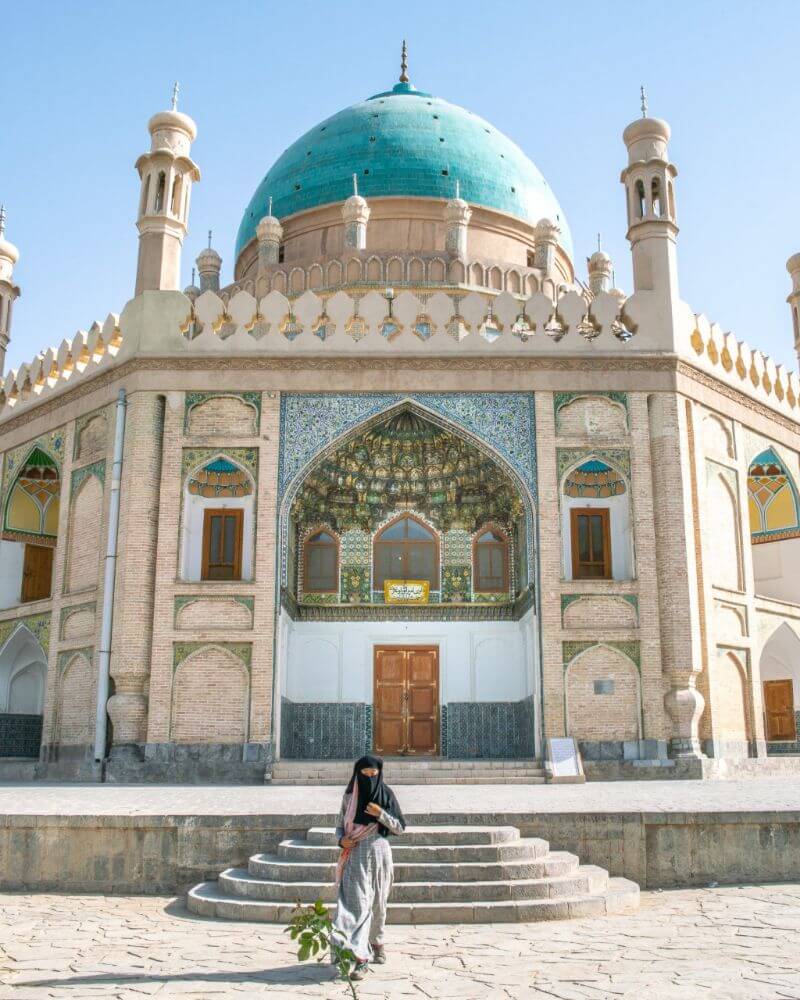 A girl wearing a niqab stands in front of a mosque in Afghanistan.