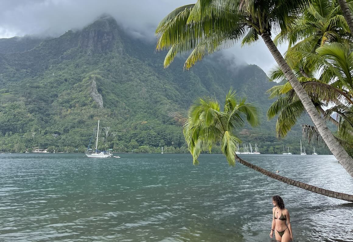 Audy poses for photo next to a beautiful palm tree and sailboat in Moorea, French Polynesia.