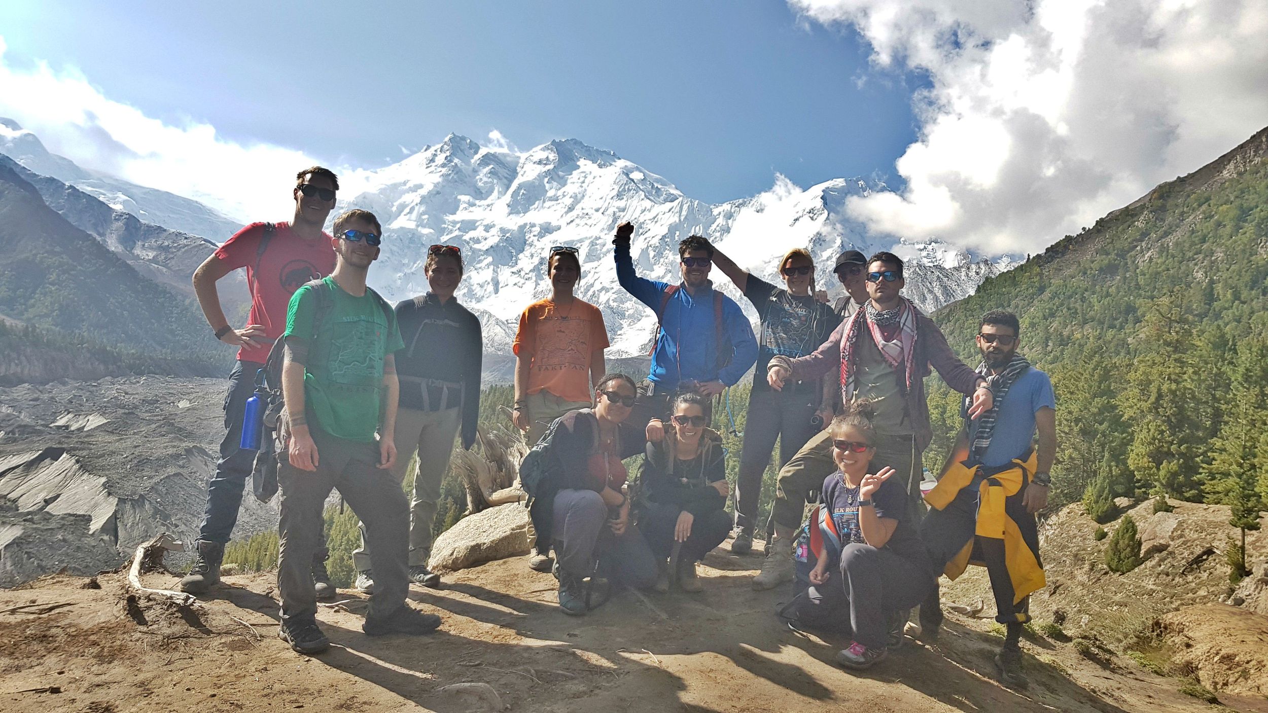 A group of people standing in a valley in Pakistan with huge snow covered mountains behind them