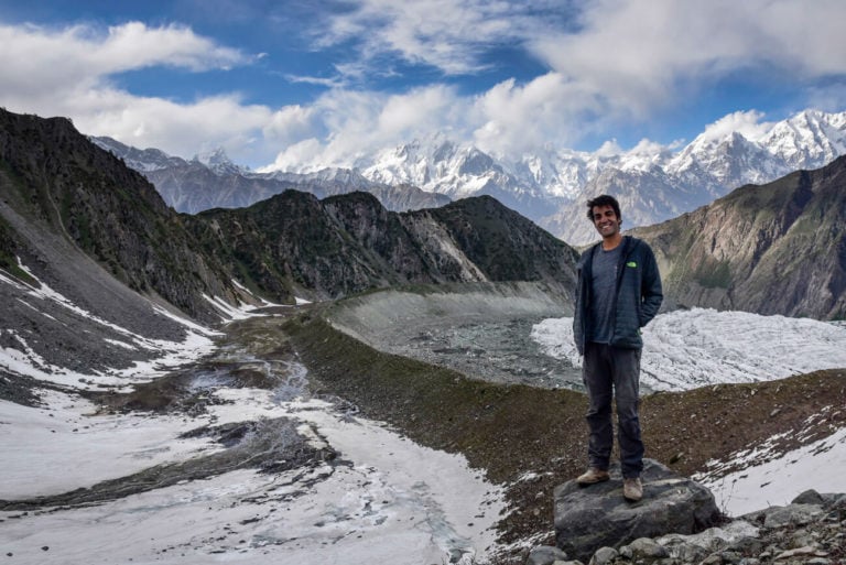 A man stands on a rock in Pakistan with mountains and glaciers behind him