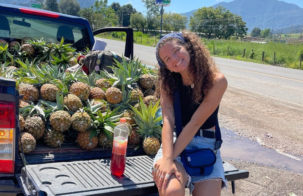 Audy sitting on the back of a pick up truck filled with pineapples whilst hitchhiking in Mexico