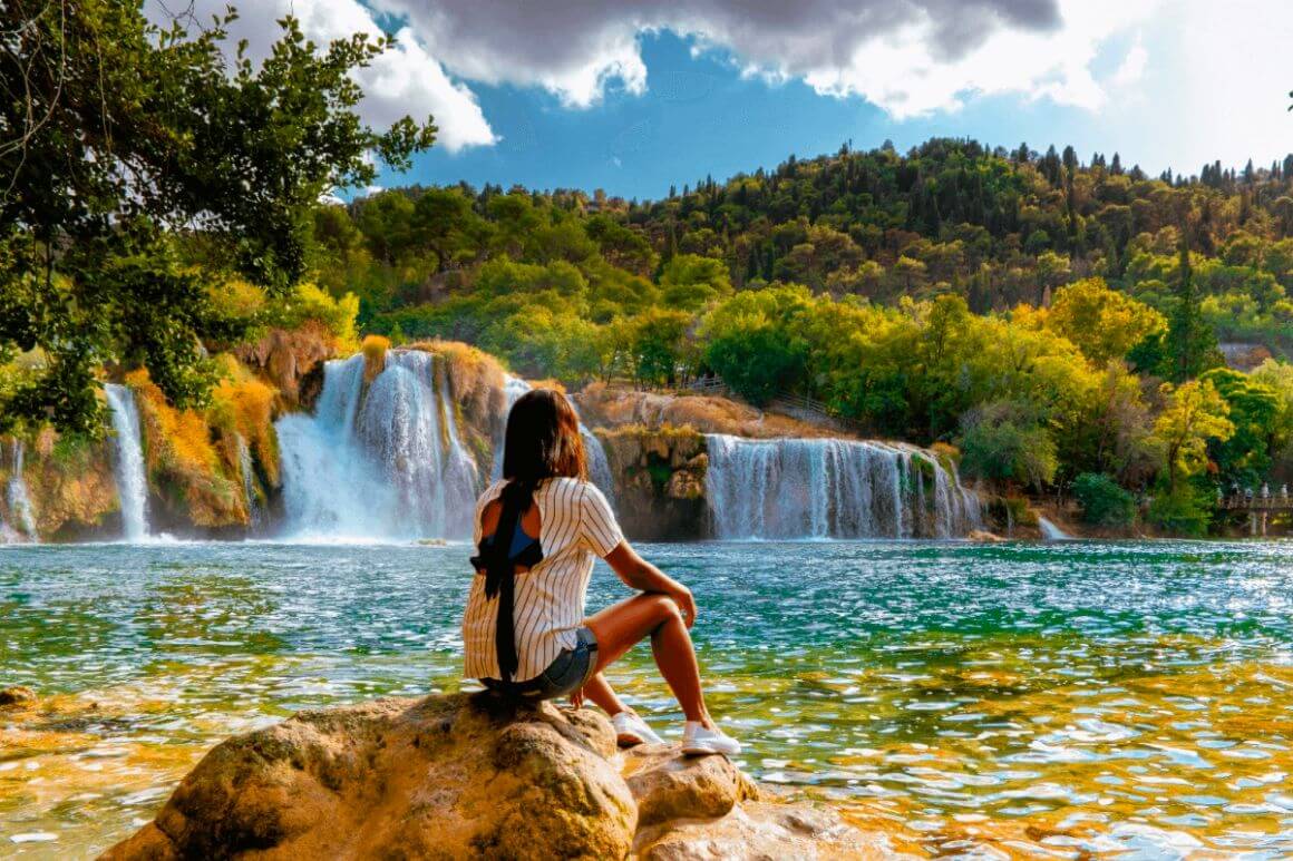 woman sitting in stone looking at krka national park waterfalls