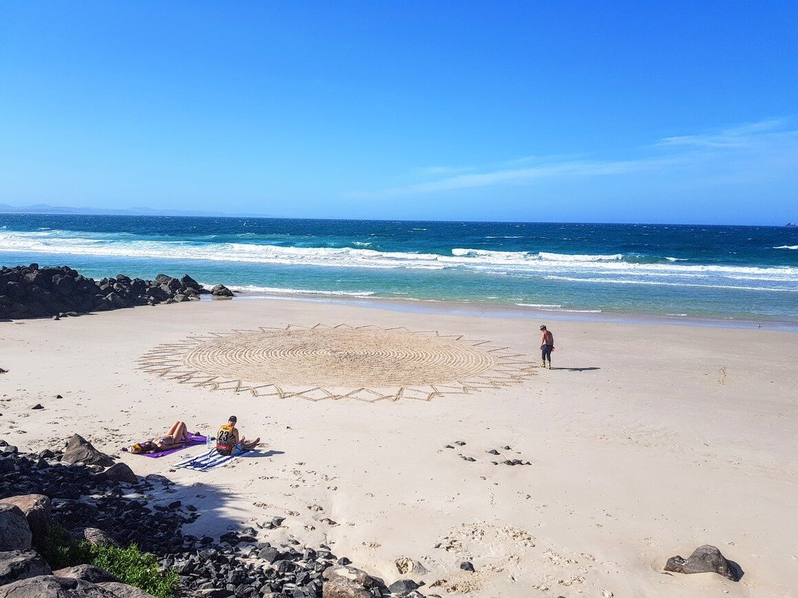 Person drawing a spiral sun in the sand by the sea