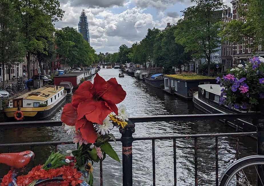 A bicycle with flowers parked on a bridge over a canal in Amsterdam.