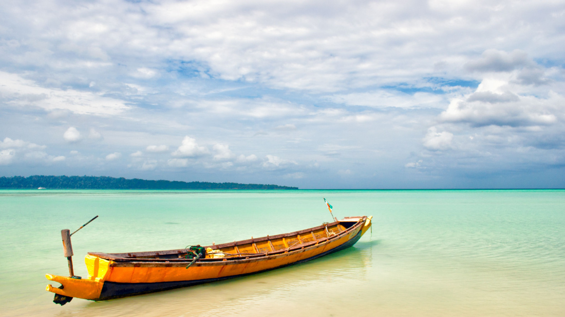 yellow long boat sitting in bright turquoise water on a white sand beach on one of India's best islands