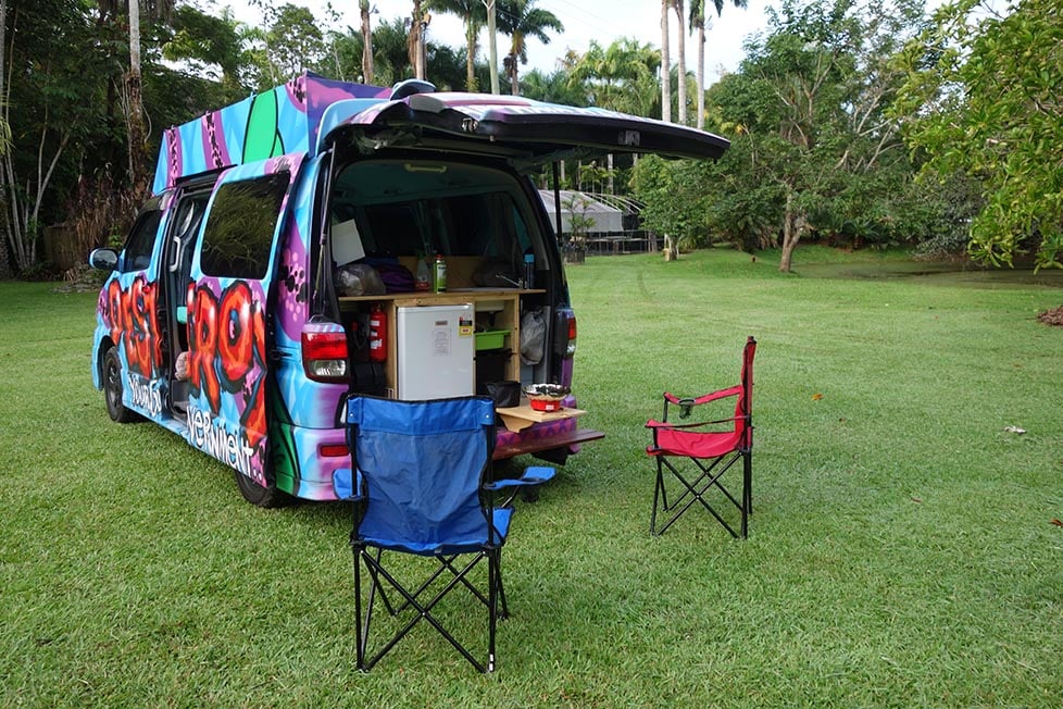 A campervan covered in cool graffiti in a palm treelined campsite