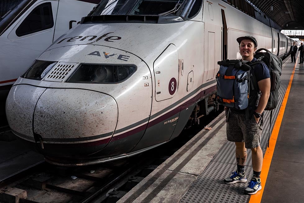 A person with two backpacks stood next to a bullet train. Wandrd Prvke backpack.