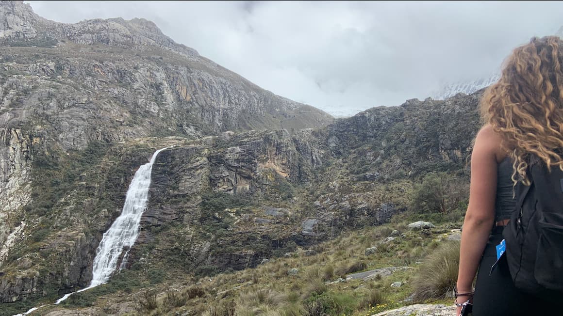 girl standing next to a waterfall while hiking in peru 