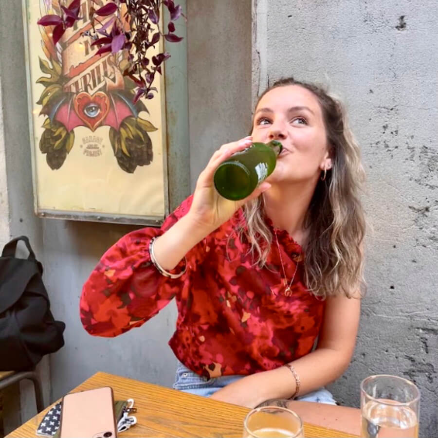 Girl swigging a beer at a cool bar with a concrete wall behind her