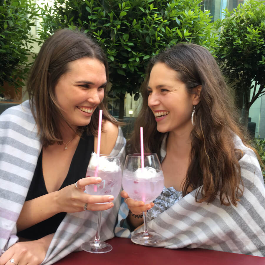 Two girls at a bar outside having a pink cocktails.