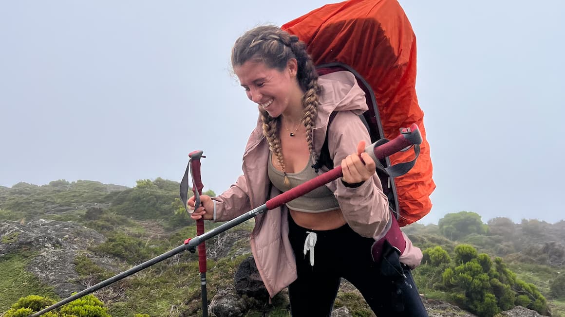 A girl trekking a mountain  with a backpack on and trekking poles in her hands