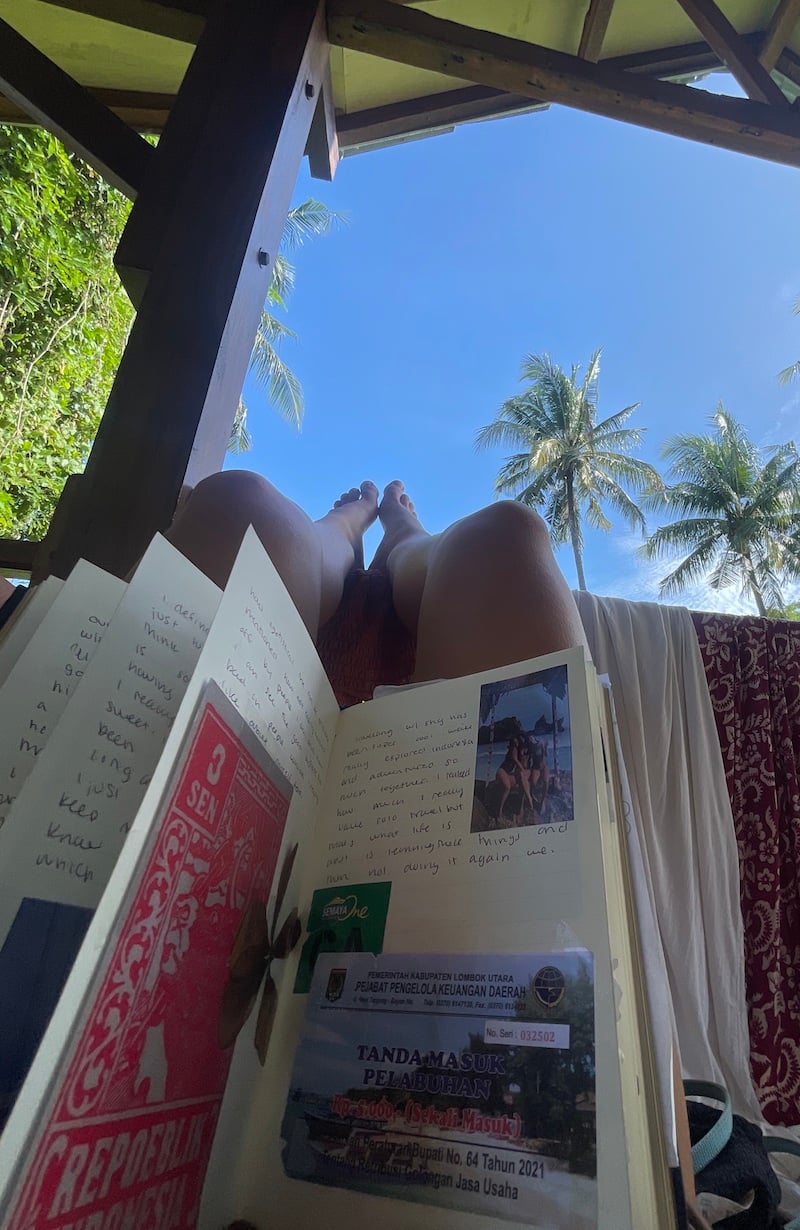a girl snaps a shot of the palm trees and a full travel journal in Lombok Indonesia.