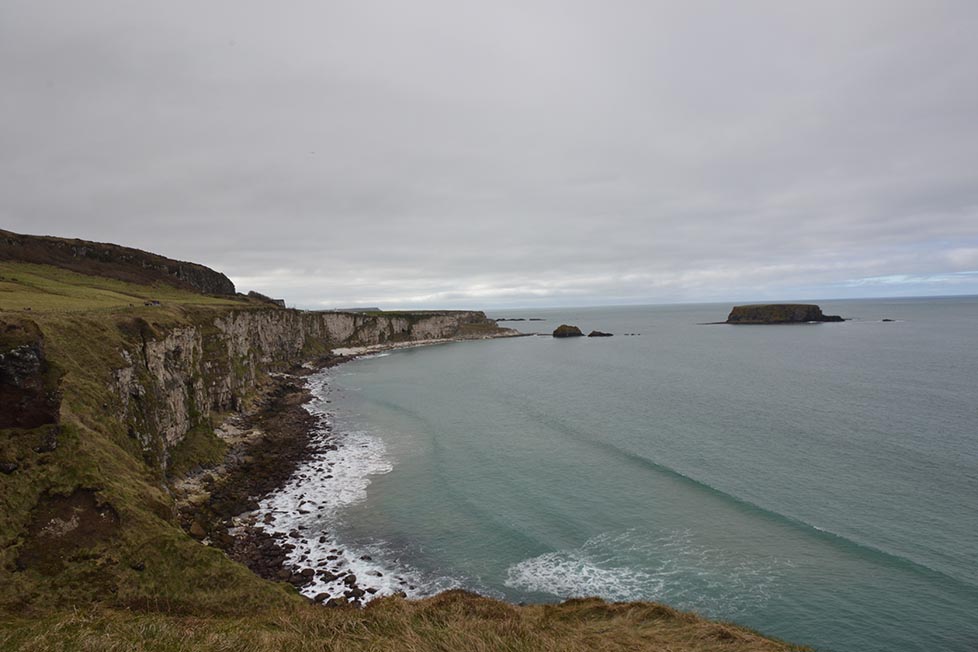 Sheer rugged cliffs and coastline dropping off to blue water on a cloudy day