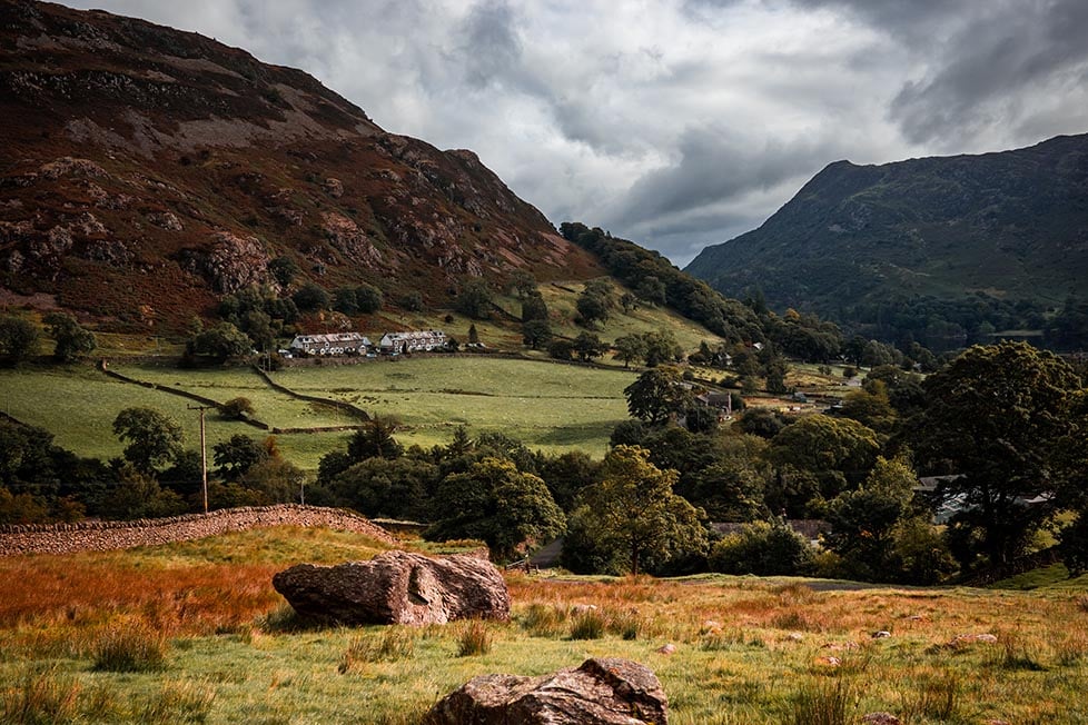 Rugged mountains and valleys with dry stone walls and a little cottage in the distance.