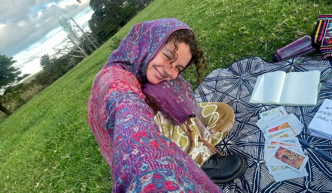 Audy smiling while journaling with tarot cards in New Zealand.