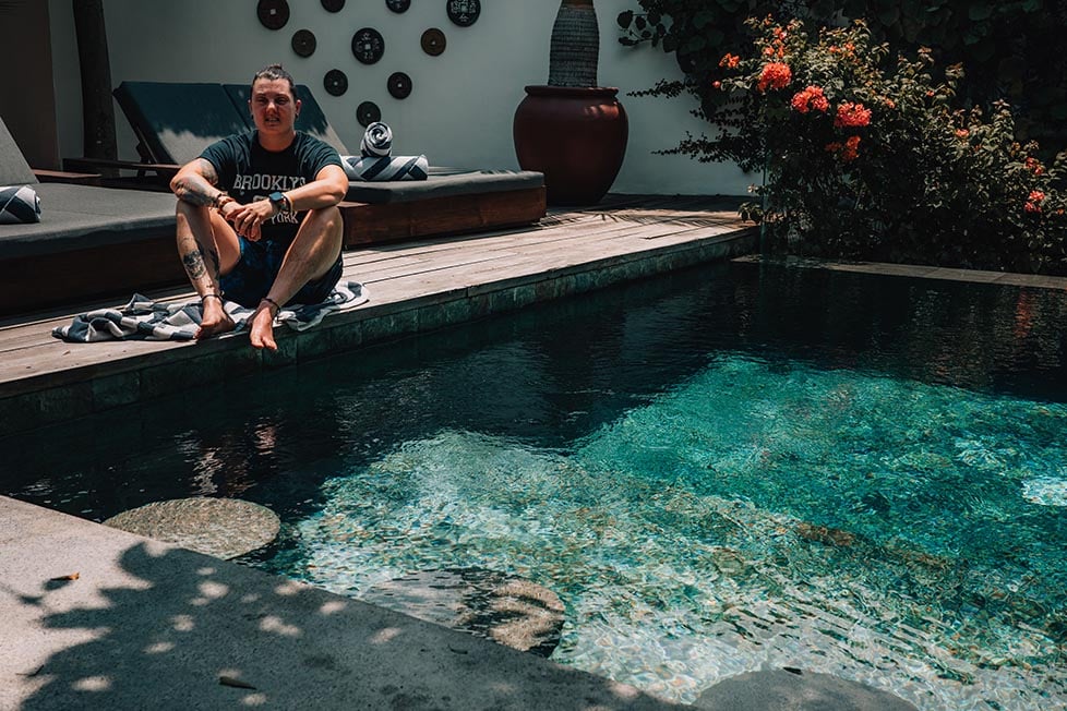 Nik relaxing on the pool deck, surrounded by a lush garden, with poolside seating in the background.