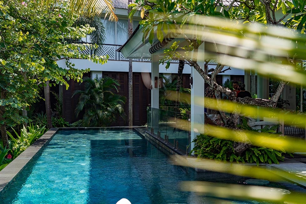 A large, rectangular swimming pool in the backyard of a two-level villa surrounded by trees.