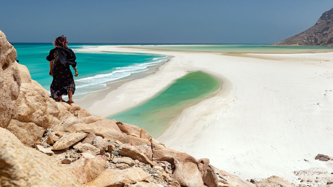 a woman standing on a rock overlooking a super bright sea in Socotra
