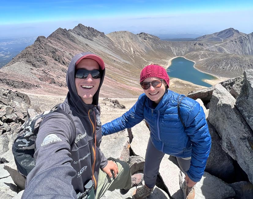 couple hiking on a mountain ridge high above a blue lake