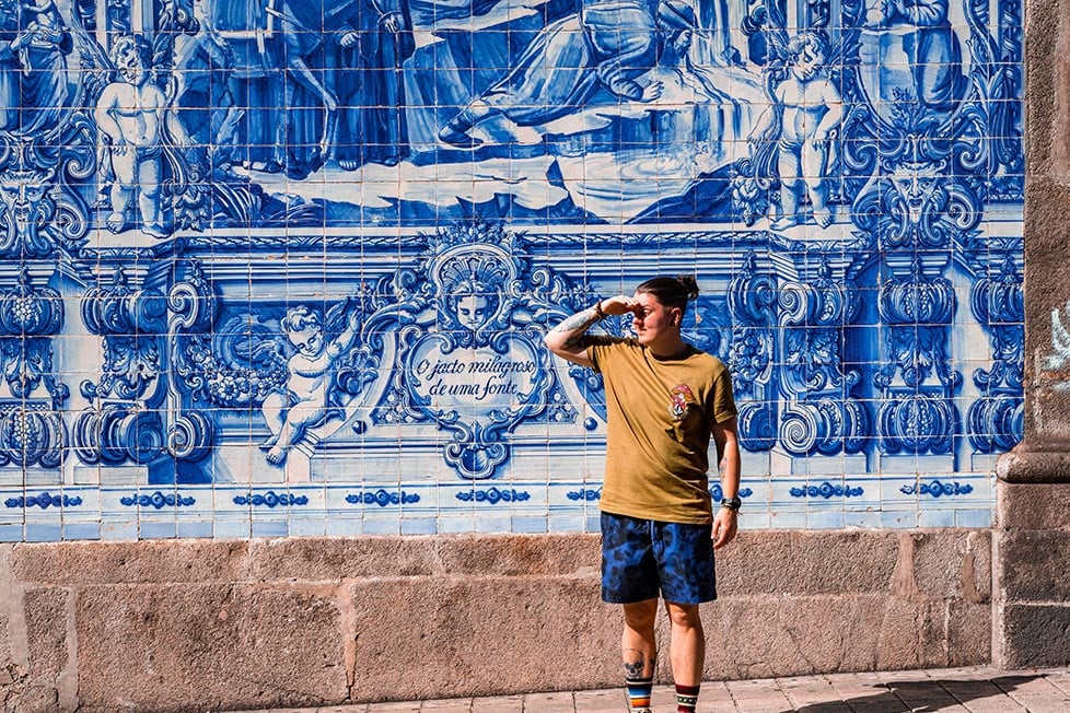 Nic covering their eyes whilst standing next to the ornate hand painted blue and white tiles of Porto, Portugal
