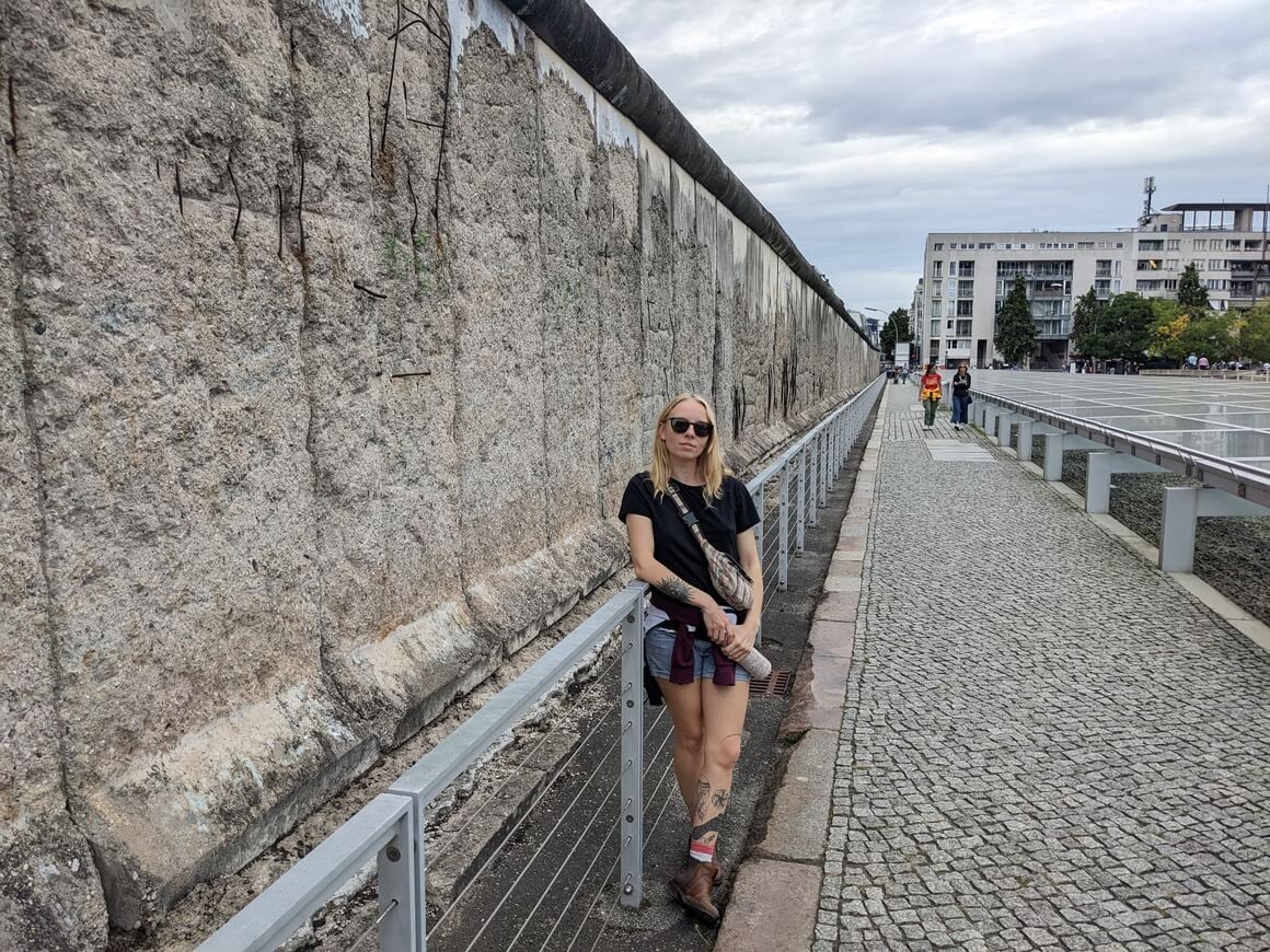 Laura stood next to the Berlin Wall in front of a barrier with a stern face