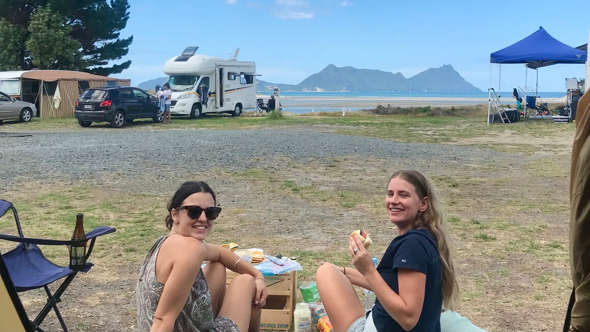 dani's friends sitting outside a tent at a campsite on the beach in new zealand