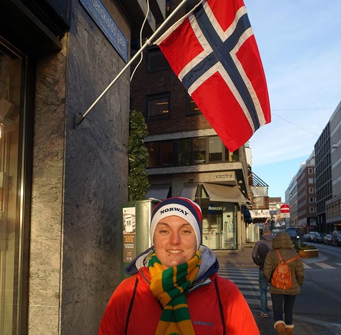 Nic standing below a Norwegian flag wearing a scarf and hat.