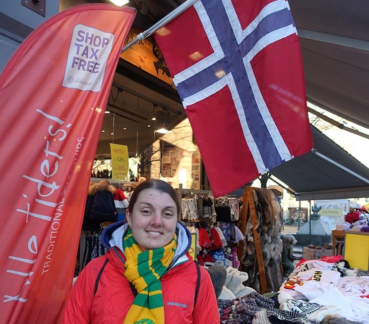 Nic standing below a Norwegian flag wearing a scarf.