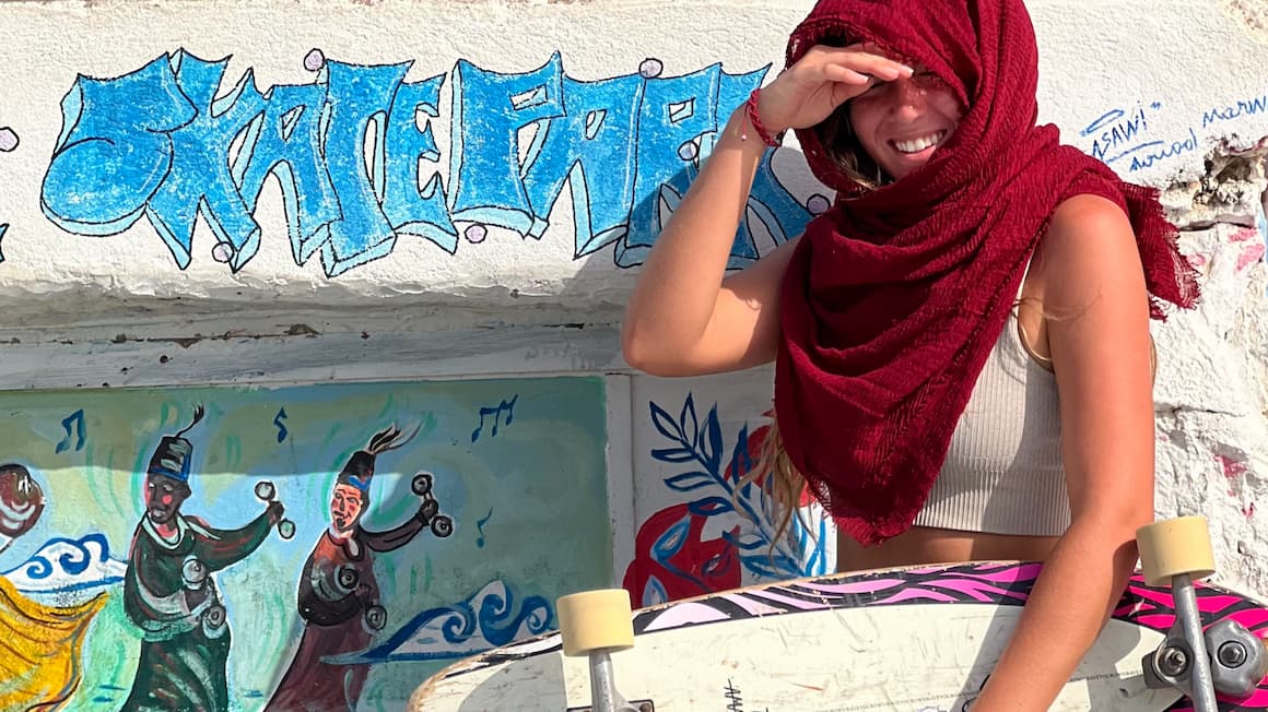 a girl wearing a red headscarf holding a skateboard at a skatepark in taghazout, Morocco 