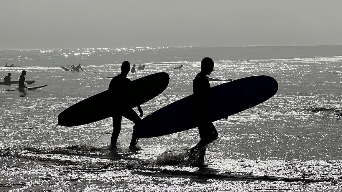 the silhouettes of two surfers walking on the beach of imsouane, morocco at sunrise 