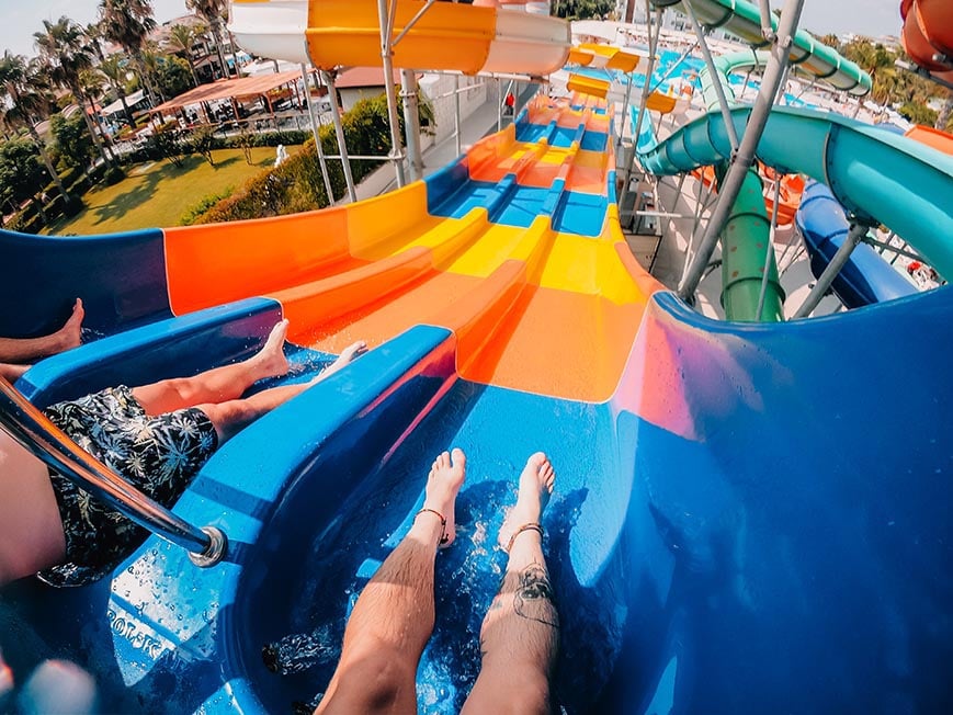 Legs of three people at the top of a waterslide at a waterpark