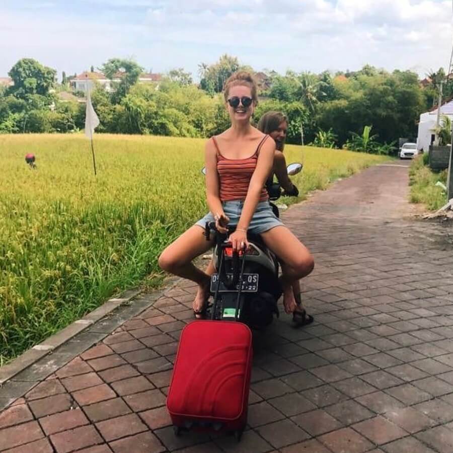 Maria and her friend transporting luggage on a scooter to the Farm Hostel in Canggu Bali with Rice Paddies next to the driveway
