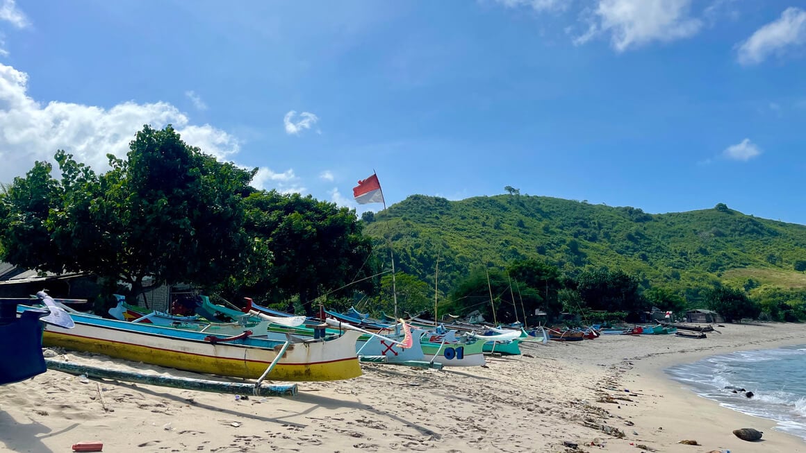 boats lining the beach at mawun beach, lombok one with an indonesian flag