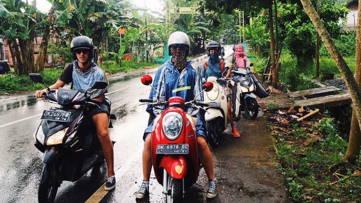 Maria and three friends with helmets on, on scooters or motorbikes in the rain on a trip from bali to lombok