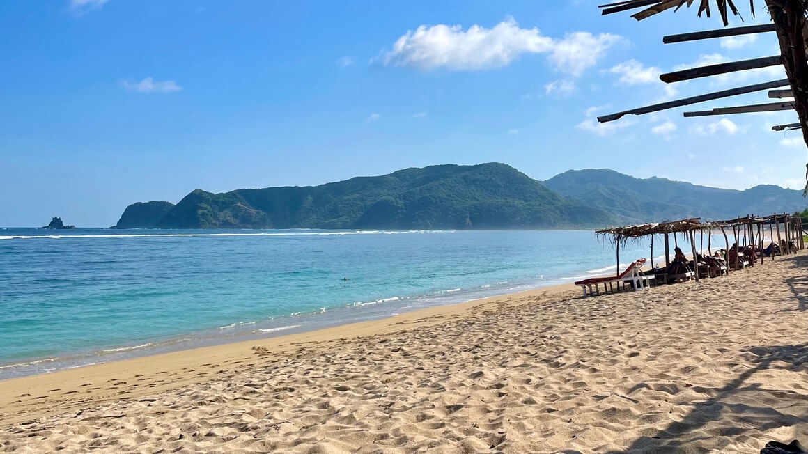 tampah beach in lombok, golden sand, warungs, bright blue sea and mountains in the background. indonesia