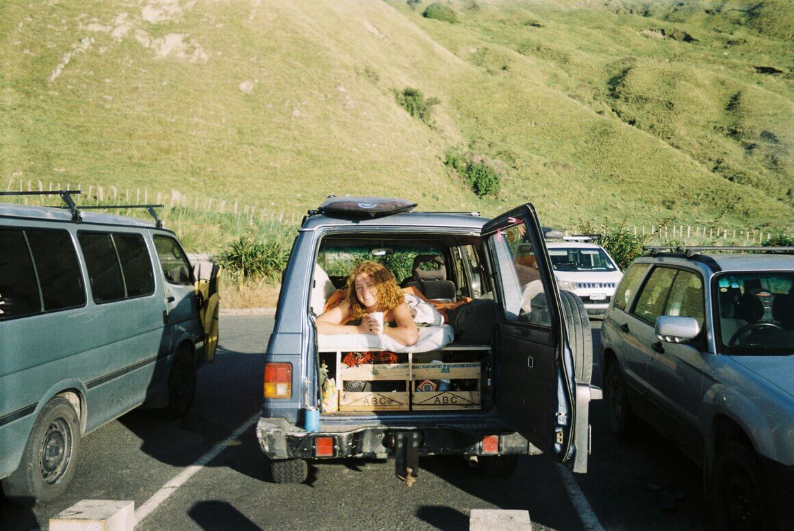 A girl drinking coffee waking up to the morning sun with a smile after camping in her car or van