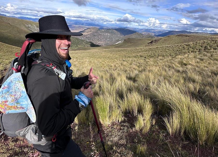 Will hiking in Peru wearing a black cowboy hat with mountains in the background and a massive smile on his face