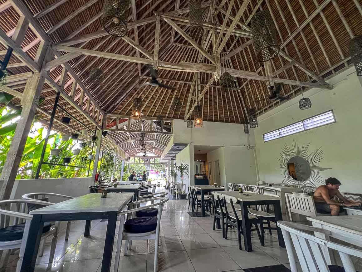 white and wood decorated cafe with high ceilings and large green plants on one of the open walls for digital nomads to cowork in